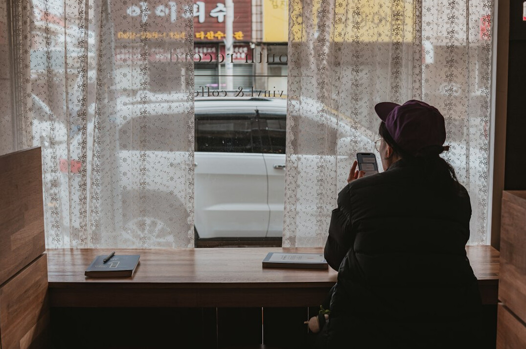 Person writing thoughtfully in a notebook by a window